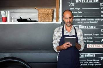 Vendedor usando una tablet mientras está de pie contra un puesto ambulante de comida