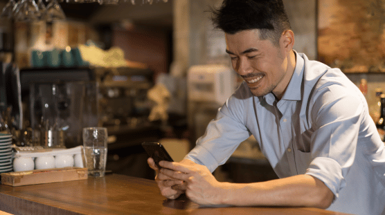 Male coffee shop owner running payroll on their mobile phone with the help of AI