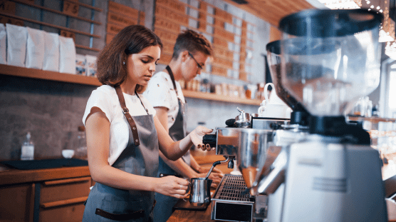 Dos empleados jóvenes preparando café latte en una cafetería.