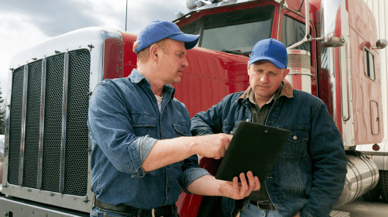 Two male truckers discussing their pay details while looking at a tablet.
