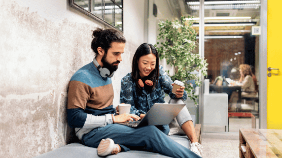 Cómo crear y administrar la nómina de una pequeña empresa Dos miembros del equipo de una compañía nueva miran una computadora portátil durante un descanso.