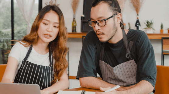 Small business owner couple using laptop discussing projects, payroll and other finances at cafe. 