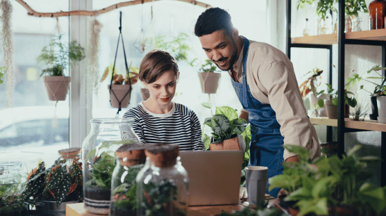 Dueños de un vivero con una laptop trabajando en una tienda de plantas de interiores.