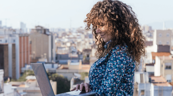 Side view of female freelancer standing on rooftop and browsing laptop while working on remote project