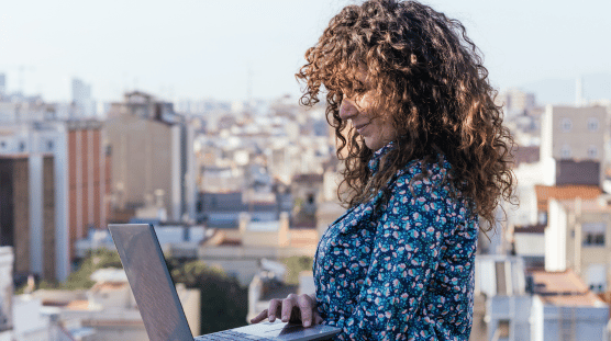 Vista lateral de trabajadora autónoma que está en la azotea con su laptop mientras trabaja en un proyecto a distancia