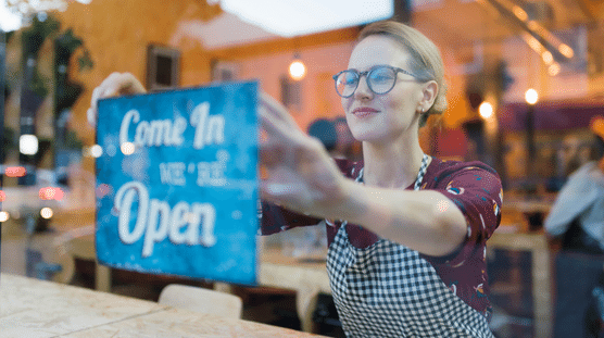 Propietaria de un negocio colocando el cartel Abierto en la ventana de una cafetería